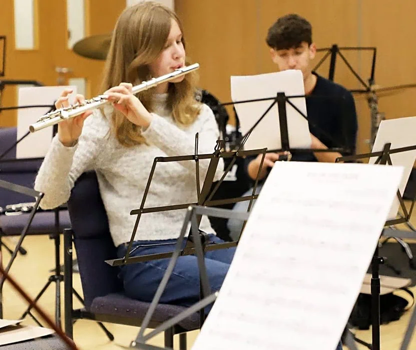 young girl playing the flute whilst reading a music sheet