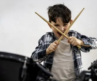 Boy with drumsticks playing drums, smiling, in a music session.