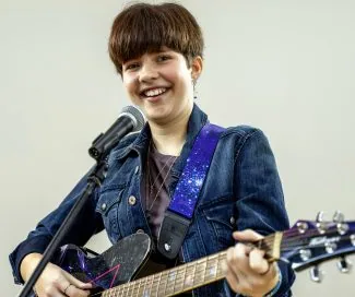 Young female musician playing guitar and singing into microphone.